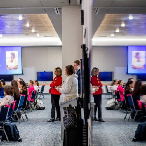 A modern conference room is filled with attendees seated at round tables, listening to a presentation titled "Keynote – Building Trust Through Responsible AI" displayed on a large screen. The room features a mirrored wall.